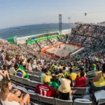 Arena de vôlei de praia montada na orla de Copacabana, no Rio de Janeiro, com arquibancadas lotadas durante competição