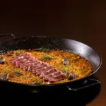Paella espanhola servida em paellera de ferro, com arroz, legumes e fatias de carne, em restaurante de hotel no Rio de Janeiro
