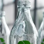 Garrafas de vidro transparentes alinhadas, com folhas verdes, representando a reciclagem e a logística reversa do vidro na hotelaria