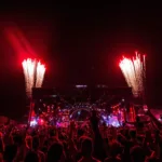 Público com os braços erguidos diante do Palco Mundo iluminado de vermelho, com fogos de artifício, durante o Rock in Rio na Cidade do Rock, no Rio de Janeiro