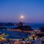 Vista noturna do Rio de Janeiro com a enseada de Botafogo e o Pão de Açúcar iluminados, cenário do turismo na cidade