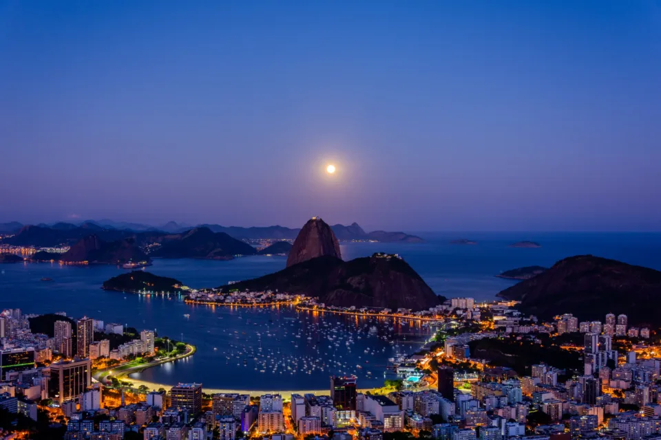 Vista noturna do Rio de Janeiro com a enseada de Botafogo e o Pão de Açúcar iluminados, cenário do turismo na cidade