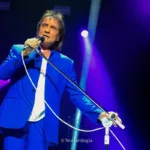 Roberto Carlos canta ao microfone durante apresentação em casa de shows, iluminado por luz de palco