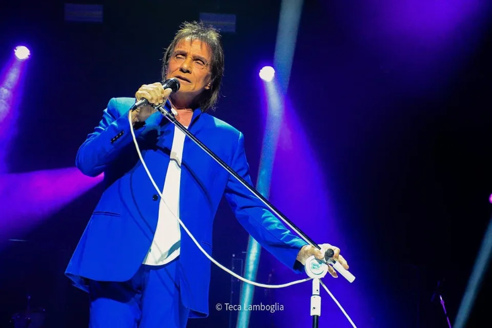 Roberto Carlos canta ao microfone durante apresentação em casa de shows, iluminado por luz de palco