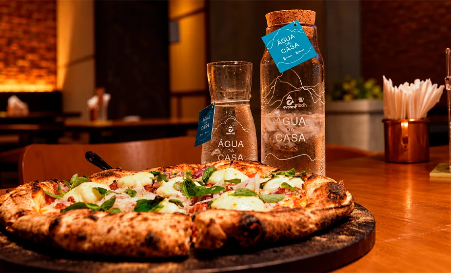 Garrafas de vidro personalizadas do projeto Agua da Casa, da Everest, ao lado de pizza napolitana na Ribalta Pizzaria, no Ribalta Hotel, na Barra da Tijuca