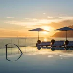 Piscina de borda infinita no rooftop do Hotel Fasano Rio de Janeiro ao pôr do sol, com guarda-sóis e espreguiçadeiras, o mar de Ipanema e o Morro Dois Irmãos ao fundo