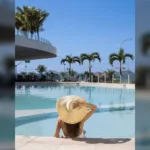 Hóspede de chapéu na piscina do Hotel Nacional, em São Conrado, com coqueiros e a cúpula do hotel ao fundo